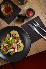cooking dish, appetizer. Salad. Restaurant serving. black dishes, wooden table.