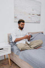 Fototapeta premium young african american man with dyed hair using smartphone while resting on bed.