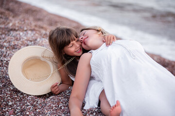 Millennial mother with daughter fooling around, having fun on the sand of the beach at sea. Little...