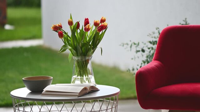 Comfortable chair , little table with book and vase of tulips on modern terrace at backyard