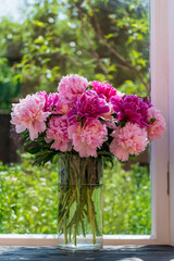Beautiful bouquet of pink peonies flowers in a glass vase on the windowsill at home, close-up
