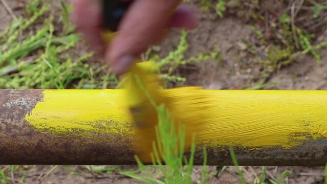 Close-up of a brush painting a pipe with yellow paint. The concept of protecting metal from corrosion, rust prevention. Household works, maintenance and repair of plumbing. UHD 4K.
