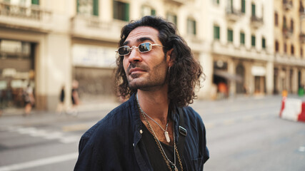 Young italian guy with long curly hair and stubble walks smiling down the street. Stylish man with...