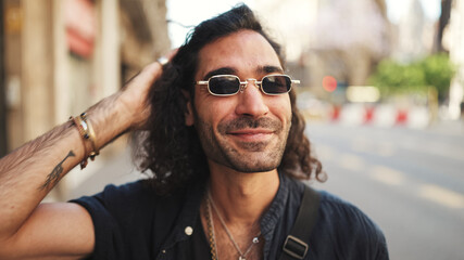 Young italian guy with long curly hair and stubble walks smiling down the street. Stylish man with...