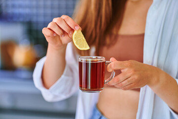 Woman drinking hot black tea with lemon slice at home kitchen