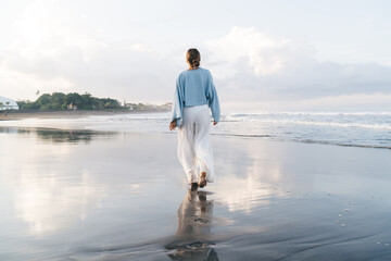 Gorgeous Caucasian woman enjoying vacations while walking on the beach feeling calm and carefree. Happy and Beautiful healthy female in white summer cloth strolls on seashore during holidays travel