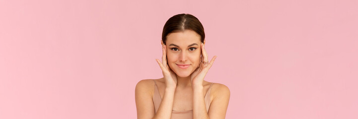 Skin care. Woman with beauty face touching healthy facial skin. Smiling female model looking at the camera and smiling over pink background. Web banner
