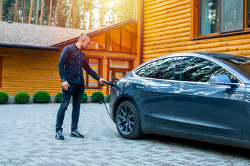 man connecting a charging cable to a car from an electric car charging station. Electric Car Being Charged. view of charging station for electric car in front yard of townhouse