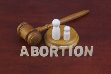 Court decision about abortion. Letters abortion with judge gavel and figures of female and child.