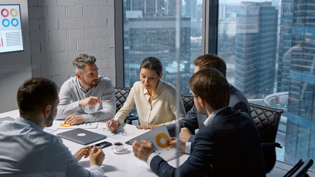 Corporate businesswoman communicating with team while sitting at desk in meeting room