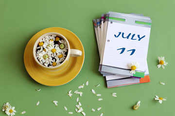 July 11 calendar: numbers 11 and name of the month july on a sheet calendar, next to a cup of chamomile tea, pastel background, top view.