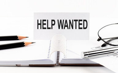 Text HELP WANTED on paper card,pen, pencils, glasses,financial documentation on table - business concept