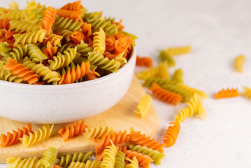 Boul with twisted colored pasta on white table. Three colors rotini or fusilli pasta in ceramik...
