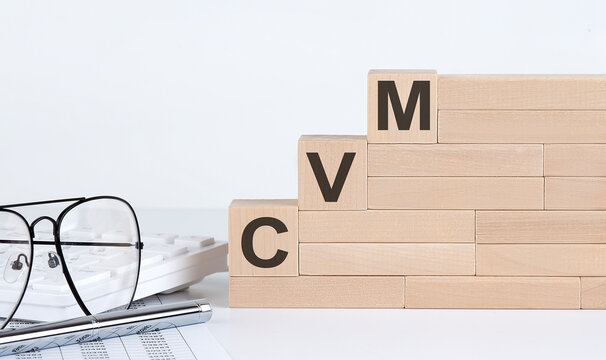 wooden cubes with letters CVM on the white table with keyboard and glasses
