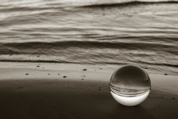 Fototapeta na wymiar Ball of glass in the sand with water in the background