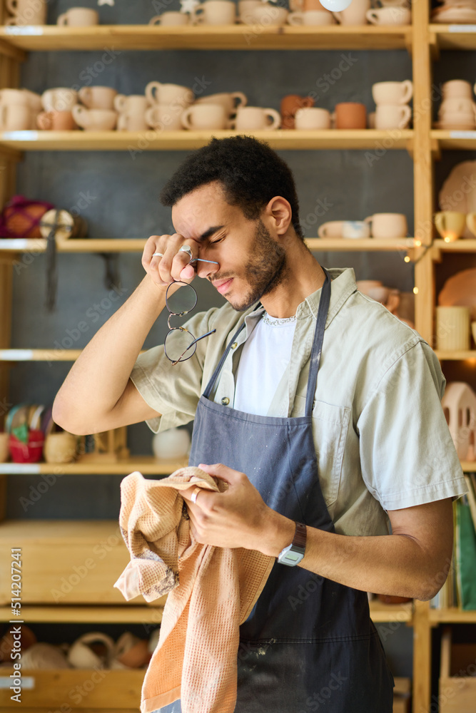 Poster young tired black man with towel touching his head after hard work over creating new handmade clay i