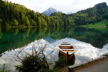 a boat resting on the tranquil, transparent emerald-green water of lake Alatsee in the Bavarian Alps reflected in the lake, Fussen or Fuessen in Bavaria, Germany	