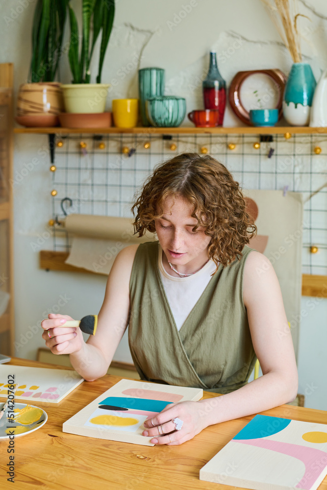 Poster creative female sitting by table in studio or workshop and creating new abstract painting with help 