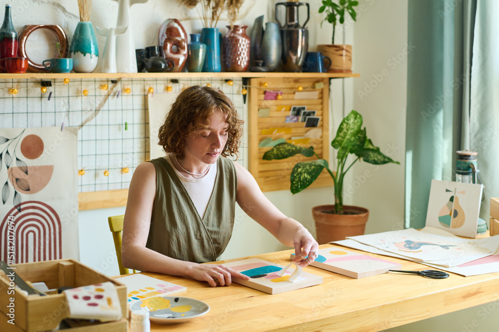 Aufkleber young creative female with paper stencil creating abstract painting while sitting by table in studio