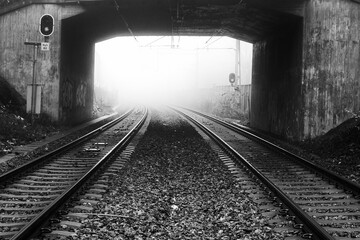 Fototapeta na wymiar Rail road tracks through a tunnel a foggy day in black and white.