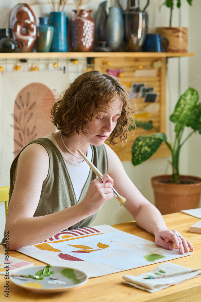 Aufkleber Young female with paintbrush over paper working over new abstract painting in workshop while using gouache of various colors