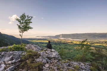 Man standing at the top of the hill and taking photos of the picturesque valley below. Vivid colors of the meadows and fields.