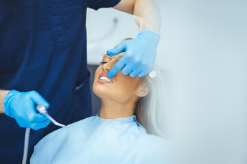 Obraz premium Pretty lady in dentist chair looking at her doctor with smile, close up. Image of pretty young woman sitting in dental chair at medical center while professional doctor fixing her teeth..