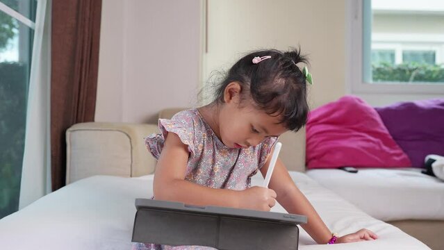 Cute little girl sitting at couch drawing picture on tablet.