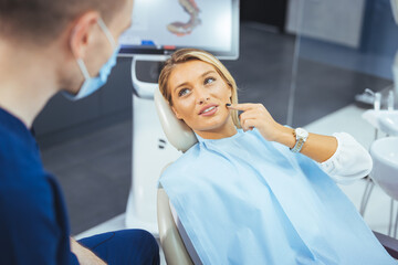 Closeup shot professional dentist with protective surgical mask, doing check up of patient. Dentist examining smiling female patient in clinic. Male is checking smiling patient in examination room.