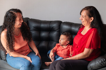 Daughter and grandson socializing with grandma. Mom and daughter laughing together on the couch at...