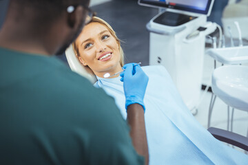 The woman came to see the dentist. She sits in the dental chair. The dentist bent over her. Happy patient and dentist concept. Amazing smile!