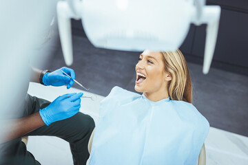 Amazing smile! Top view of dentist examining his beautiful patient in dentist’s office. Dentist examining teeth of her female patient during appointment at dental clinic. Focus is on young woman
