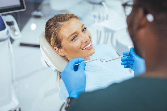 Pretty lady in dentist chair looking at her doctor with smile, close up. Image of pretty young woman sitting in dental chair at medical center while professional doctor fixing her teeth..