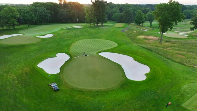 Establishing shot of golf course at sunrise. Beautiful aerial view of green being mowed and tended to.