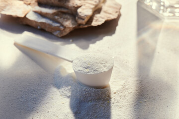 Sport food supplement powder with natural beige background and props. Still life: supplement, creatine, hmb, bcaa, amino acid or vitamine in a white scoop. Sport nutrition and healthy life concept