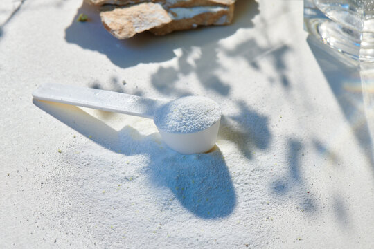 Sport food supplement powder with natural beige background and props. Still life: supplement, creatine, hmb, bcaa, amino acid or vitamine in a white scoop. Sport nutrition and healthy life concept