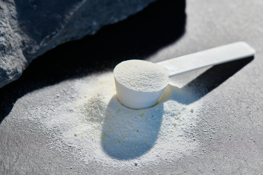 Sport food supplement powder with natural beige background and props. Still life: supplement, creatine, hmb, bcaa, amino acid or vitamine in a white scoop. Sport nutrition and healthy life concept