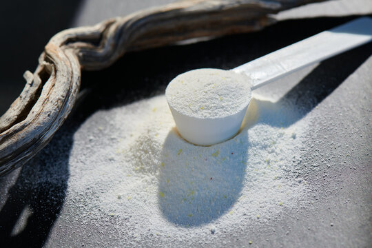 Sport food supplement powder with natural beige background and props. Still life: supplement, creatine, hmb, bcaa, amino acid or vitamine in a white scoop. Sport nutrition and healthy life concept