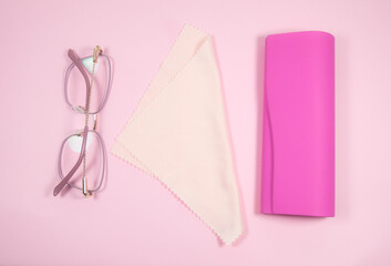 Pink frame womens glasses with glasses cleaning cloth and case on a pink background.