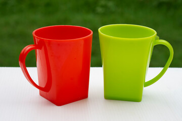Red and green plastic mugs with handle on white table outdoor. Concept :Plastic product used for contain water or beverage to drink in everyday life. Light and not easy breakable as glass. Kitchenware