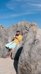 Hombre blanco barbudo leyendo un libro entre rocas en playa rocosa