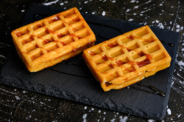 Sweet waffles poured with honey on a slate board.