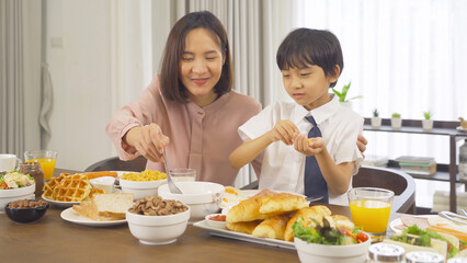 Portrait of happy smiling Asian Family eating breakfast food together before the child going to school at home. Family relationship. Love of mother, and son. People lifestyle.