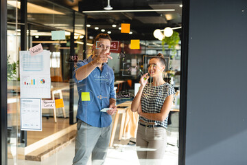 Creative caucasian businessman discussing business strategy with biracial businesswoman in office