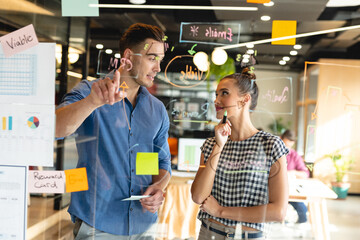Creative caucasian businessman discussing business strategy with biracial businesswoman in office