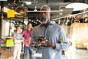 African american mature businessman analyzing charts on glass wall in creative office
