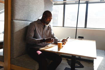 African american mature businessman using smart phone while having coffee during break in office