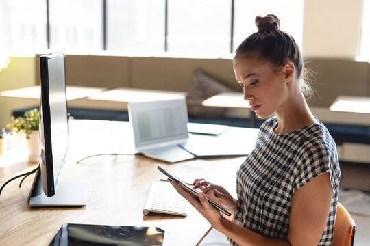 Side view of biracial young businesswoman using digital tablet while sitting in creative office