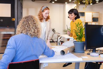 Multiracial female and male colleagues discussing over blueprint at desk in creative office