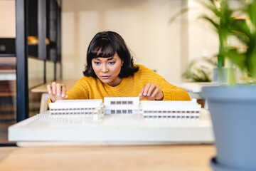 Biracial young female architect examining architectural model in creative office